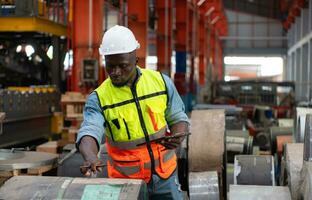Front view of young man worker using digital tablet to check stock in metal sheets storage of factory photo