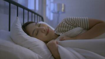 asiático joven mujer giro apagado el cabecera ligero y luego su dormir en un suave almohada foto
