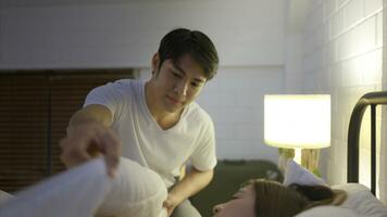 Young Asian man covers his wife with a blanket as she sleeps on the bed. photo