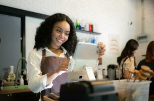 Portrait of smiling waitress using digital tablet in coffee shop with colleagues in background photo