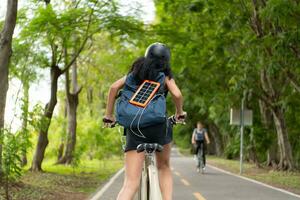 Rear view of Asian woman riding a bicycle in the park. It has a backpack with a solar panel for charging smartphone. photo