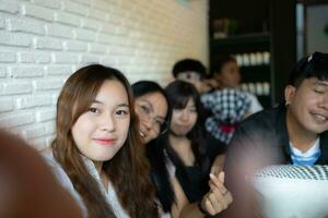 Group of asian friends sitting on sofa in cafe and taking selfie with smartphone photo