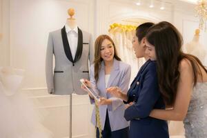 In a wedding dress shop, an Asian LGBT couple looks at the groom's suit to wear on his wedding day. photo