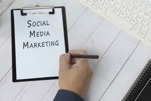 Hand with pencil writing the words Social Media Marketing on a paper with black clipboard. photo