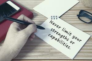 Motivational quote on notepad. Never limit your strengths or capabilities. photo