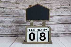 Chalkboard with February 08 date on white cube block on wooden table. photo