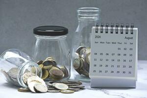 August 2024 calendar and glass jars with multicurrency coins. photo