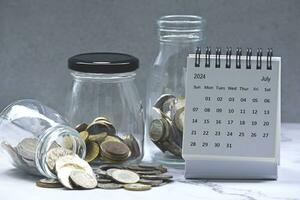 July 2024 calendar and glass jars with multicurrency coins. photo