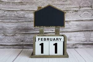 Chalkboard with February 11 calendar date on white cube block on wooden table. photo