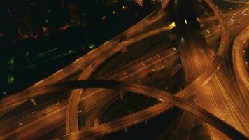 Illuminated multi-level road interchange and cars traffic at night. Drone is flying forward, camera is tilting down. Aerial view.. video