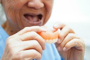 Asian senior woman patient wearing teeth denture into her mouth for chew food. photo
