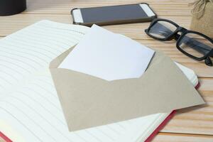 Card in brown envelope with notepad, smartphone, reading glasses on wooden desk. photo