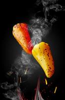 Two grilled peppers hovering over flames in sparks and haze on black background photo