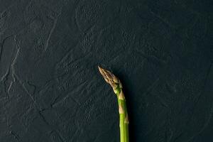 One raw fresh green asparagus stalk over black slate background. Concept of food and seasonal vegetables crop. Close up, copy space photo
