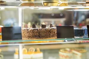 Closeup of chocolate cake behind glass of showcase in pastry shop photo