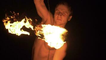 Muscular Man is performing trick on fire show. Two fireballs on chains are spinning around. Slow motion. video