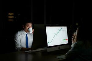 Both of young Asian broker international stock traders working together on desktop at night office, International financial investment company concept photo