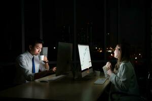 Both of young Asian broker international stock traders working together on desktop at night office, International financial investment company concept photo