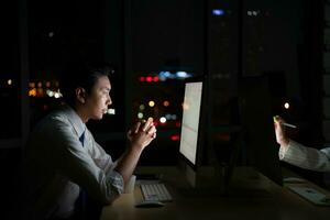 Young Asian broker international stock traders working at night in office using computer and thinking. photo