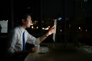 Young Asian broker international stock traders working at night in office using computer and thinking. photo