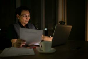 retrato de joven asiático negocio hombre trabajando en ordenador portátil en noche a oficina foto