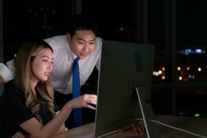 Both of young Asian broker international stock traders working together on desktop at night office, International financial investment company concept photo