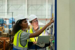 Portrait of two female engineers using laptop while standing in factory, To check the operation of the machine's circuit board. photo