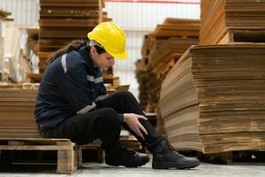 Warehouse worker sitting on the floor in front of stack of cardboard boxes with pain in his leg from hitting wooden pallets. photo