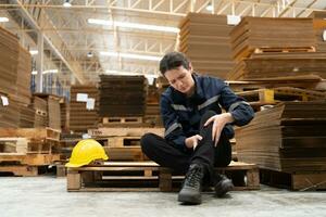 Warehouse worker sitting on the floor in front of stack of cardboard boxes with pain in his leg from hitting wooden pallets. photo