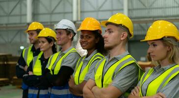 Group of diverse factory workers standing in a row and young female in center looking at camera photo