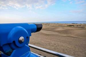 a blue binoculars on a rail overlooking the ocean photo