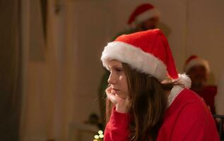 Portrait of teenage girl in Santa hat sitting on chair in front of Christmas tree, Merry Christmas and Happy Holidays photo