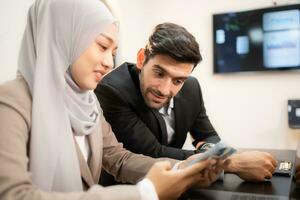 In a modern office, a hijab businesswoman and a businessman talking and use a smart phone while in a meeting. photo