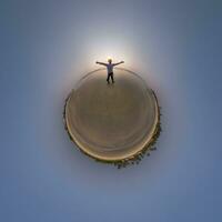 tiny planet in blue sky with happy man joyfully stands on seashore in rays of evening tropical sun with transformation of spherical panorama 360 degrees. Curvature of space. photo