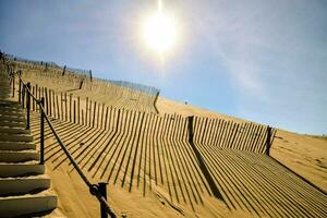 the sun shines brightly on a sand dune with fences photo