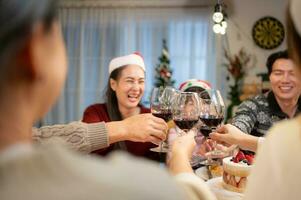 Happy asian family celebrating Christmas together at home. Cheerful senior parents and children in Santa hat clinking glasses of red wine. photo