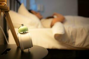 Alarm clock on a bedside table with woman sleeping in the background photo