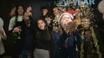 nuevo año fiesta, grupo de joven personas en Papa Noel sombreros soplo papel picado mientras celebrando nuevo año foto