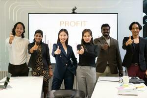 A group of multiracial businesspeople gives the thumbs up in front of the meeting room, indicating the concept of business success. photo