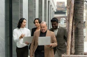 Group of business people walking and working on laptop computer in side of modern office building. Multiethnic group of business people using digital devices outdoor. photo