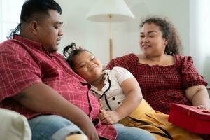 A plus size family with a father wearing a prosthetic leg, Give a gift to a daughter who does well in school and receives acclaim from her teachers, in the living room of the house. photo