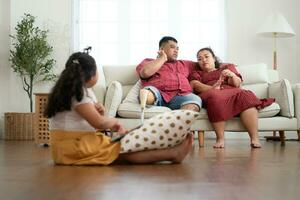 A plus size family with a father wearing a prosthetic leg, During rest time allow daughter to play games on tablet in the living room of the house. photo