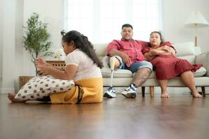 un más Talla familia con un padre vistiendo un protésico pierna, durante descanso hora permitir hija a jugar juegos en tableta en el vivo habitación de el casa. foto