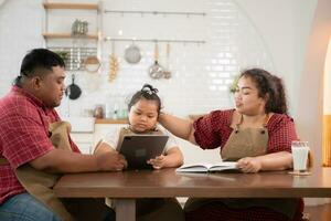 A plus-size family with a father wearing a prosthetic leg, is happily assisting a child with her homework and having fun together in the dining room of the house before cooking together photo