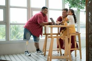 A plus-size family with a father wearing a prosthetic leg, is happily assisting a child with her homework and having fun together in the balcony of the house photo