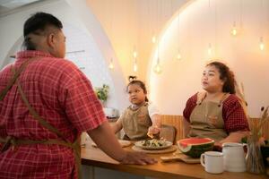 un talla extra familia con un padre vistiendo un protésico pierna, comer juntos después Cocinando y hija bebidas Leche para salud en el comida habitación de el casa foto