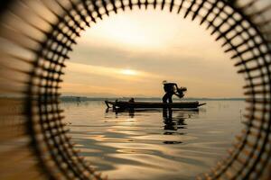 silueta de pescador a amanecer, en pie a bordo un remo barco y fundición un red a captura pescado para comida foto