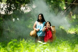 Two girls Asian women with traditional clothing stand in the rainforest. They had fun playing together before assisting Grandpa in catching fish in a nearby lake. photo