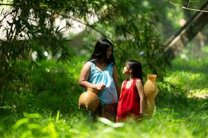 Two girls Asian women with traditional clothing stand in the rainforest. They had fun playing together before assisting Grandpa in catching fish in a nearby lake. photo