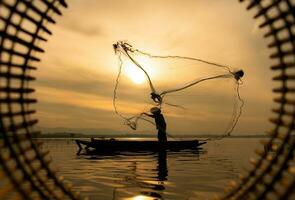 Silhouette of fisherman at sunrise, Standing aboard a rowing boat and casting a net to catch fish for food photo